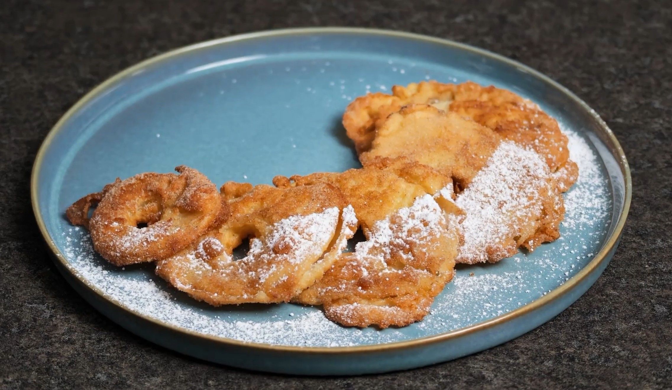 Apfelradln dusted with icing sugar on a blue plate